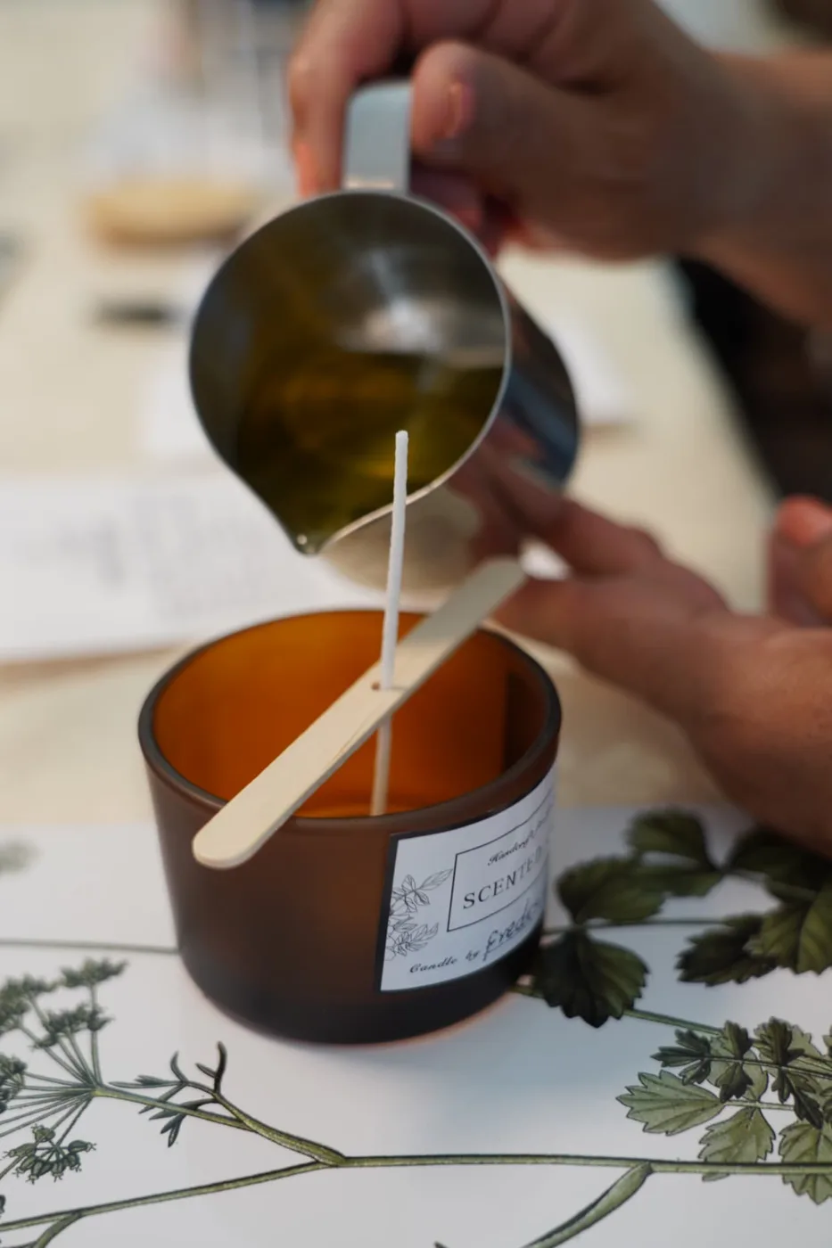 Wax being poured into a labelled candle vessel during a workshop