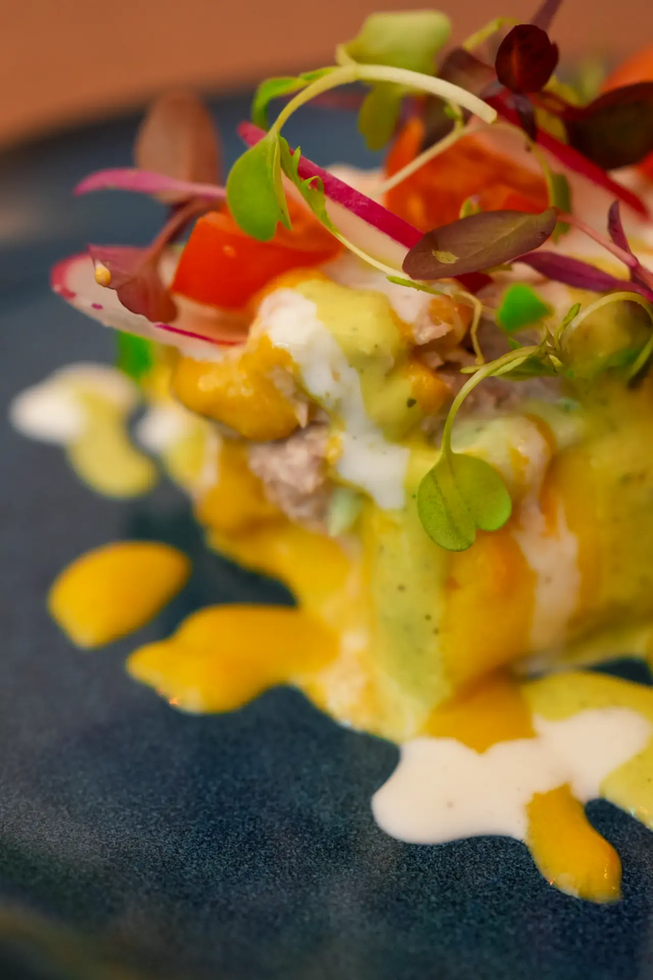 Close-up of a layered causa with sauces, tomato and microherbs at Maka