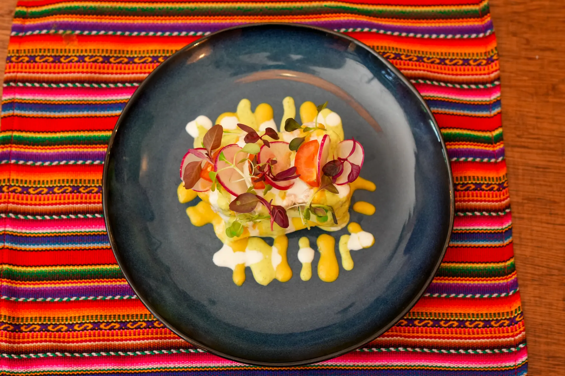 Maka's causa plated from above on a deep blue plate over a woven Andean textile