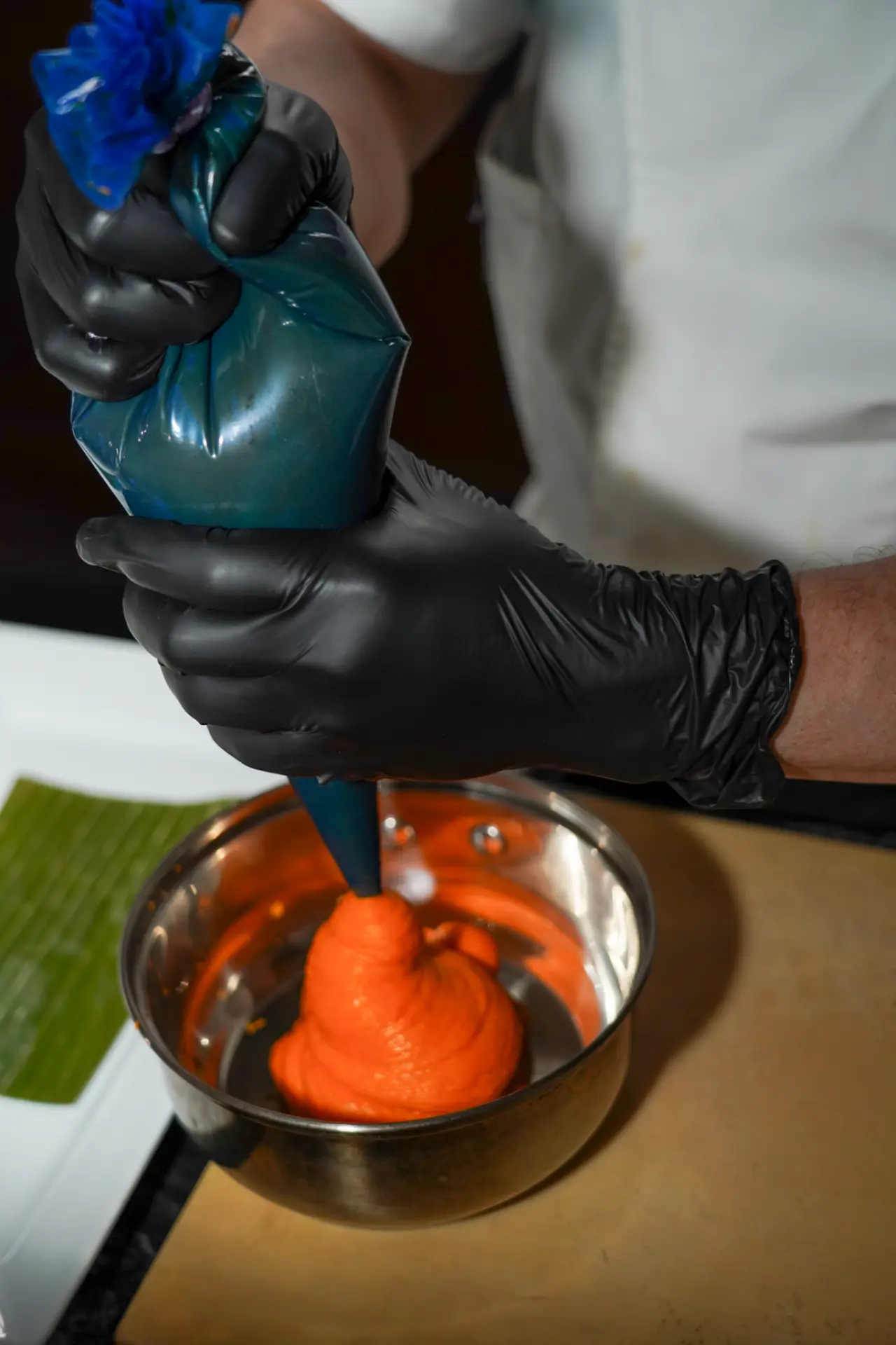 Chef piping a bright orange purée from a pastry bag while preparing a competition dish
