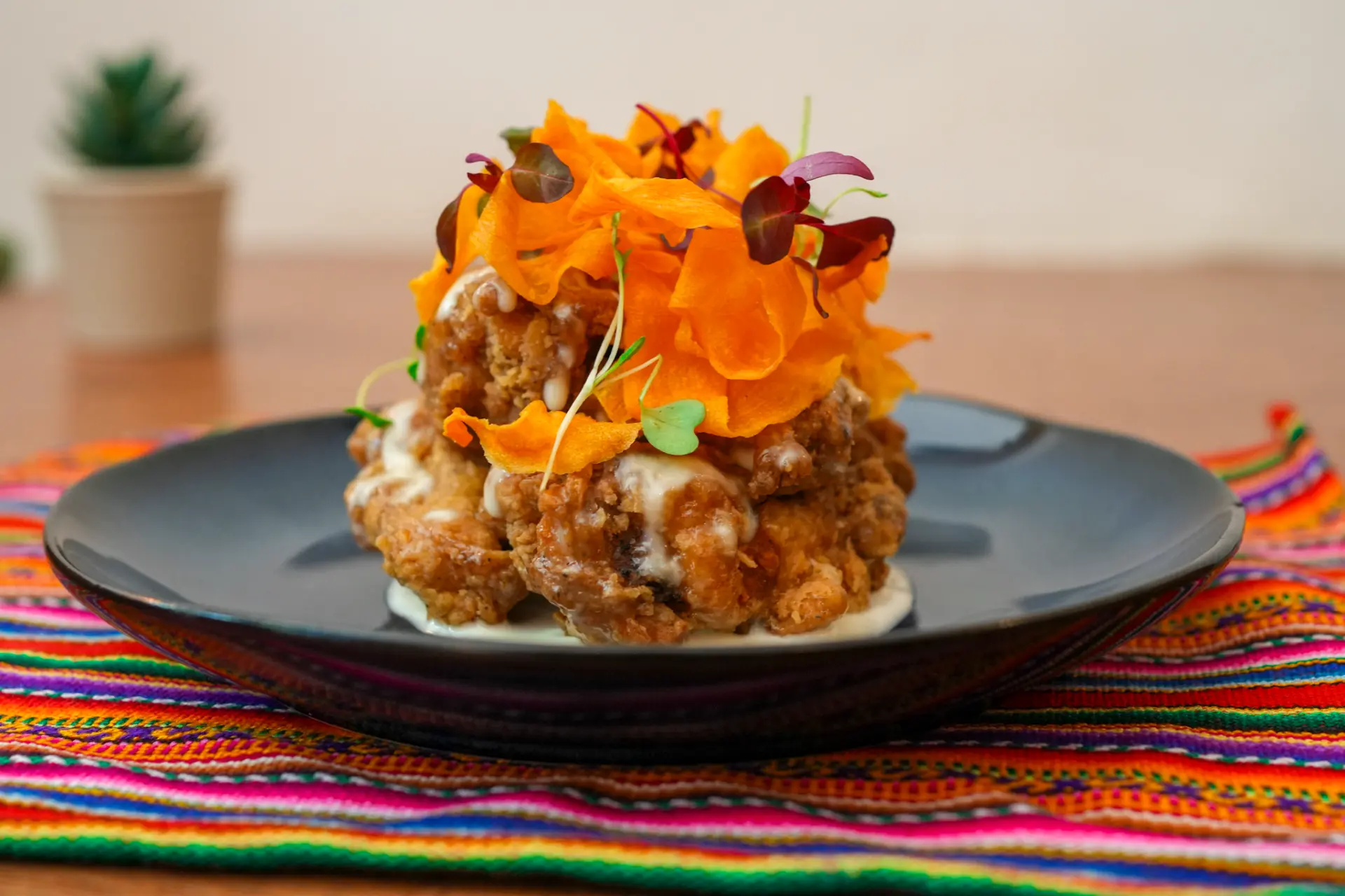 Maka's jalea plated on a dark ceramic dish with crisp carrot ribbons and microherbs