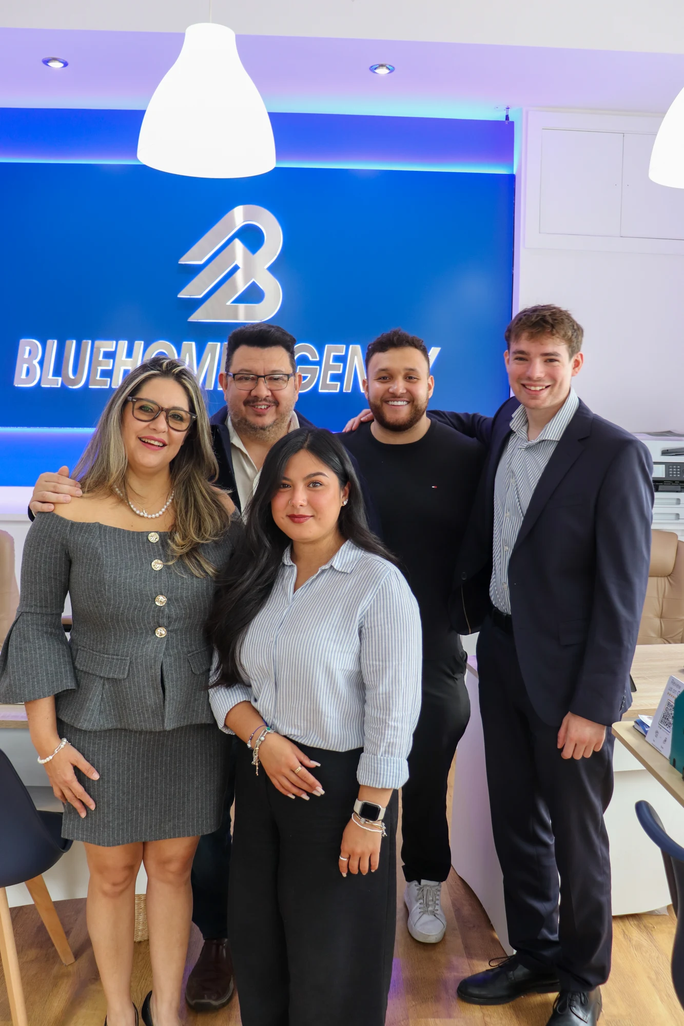 The five-person BlueHome team standing together in the agency office, in front of the illuminated BlueHome Agency sign