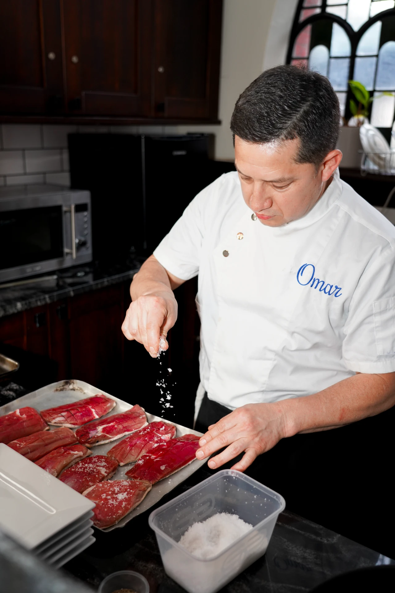 Chef Omar of Colibrí seasoning duck breasts in the kitchen before service