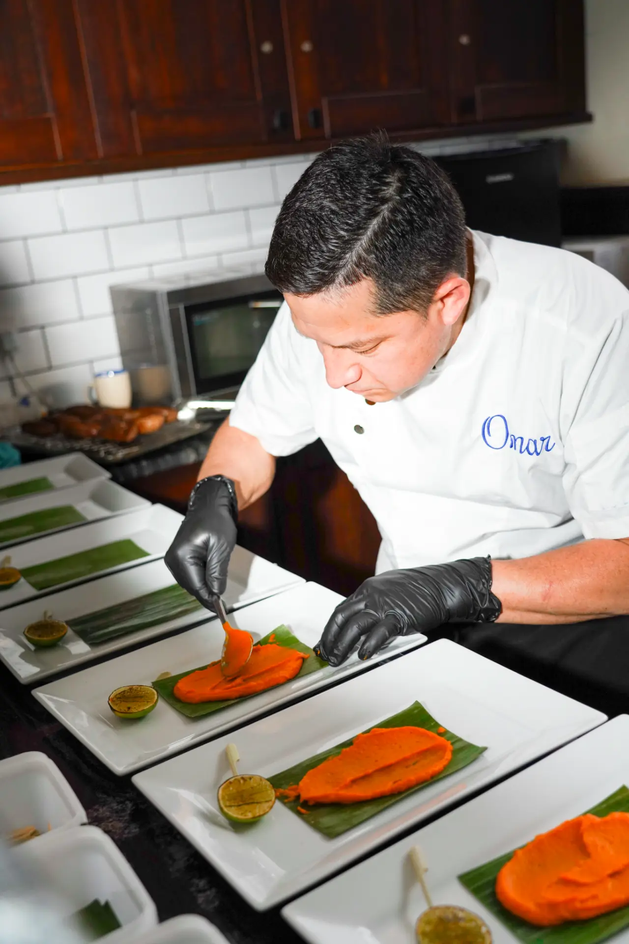 Chef Omar of Colibrí spreading purée onto banana leaf across a line of plates